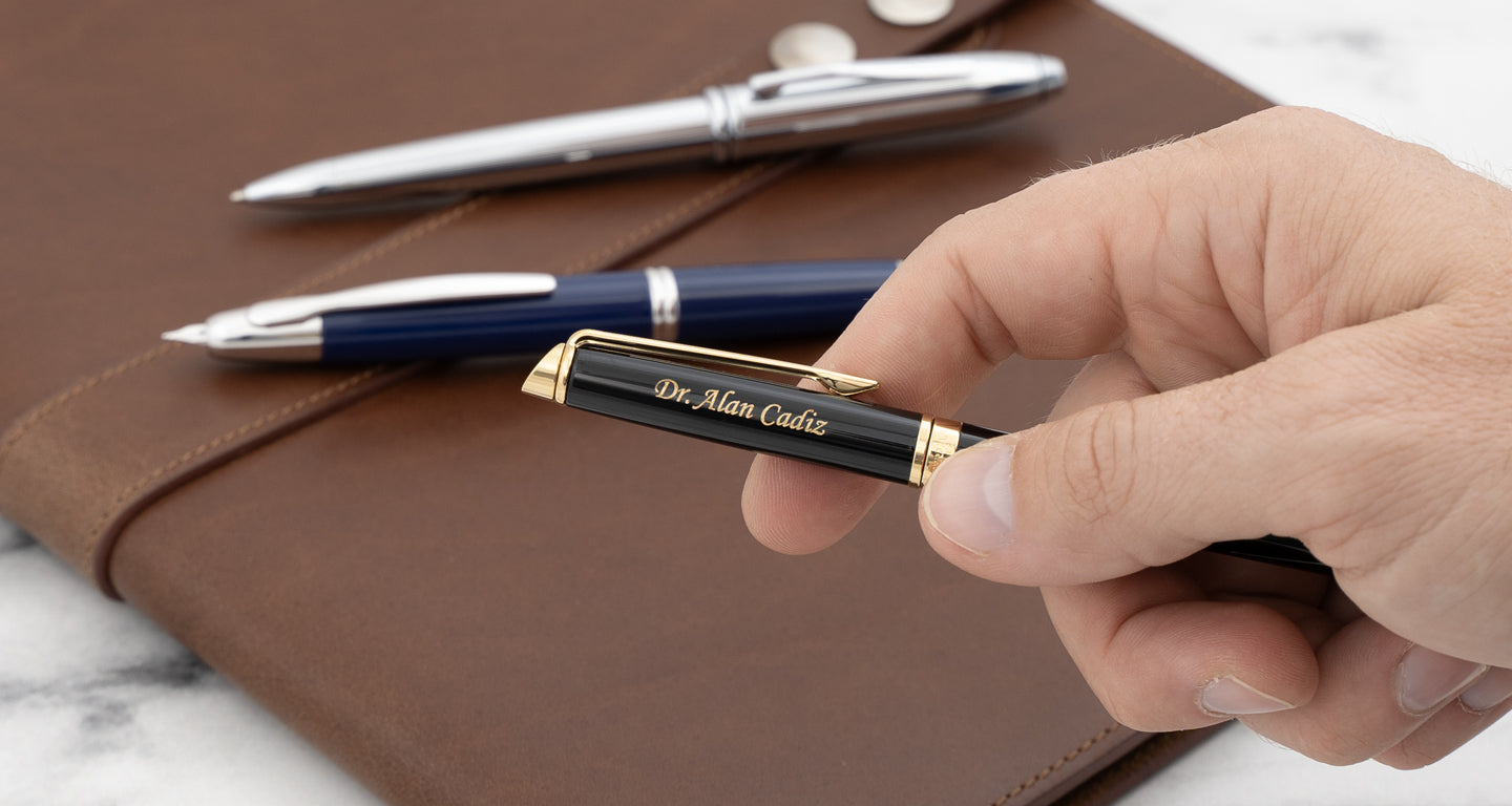 waterman hemisphere rollerball pen with engraving held in hand with a pilot vanishing point and a cross townsend